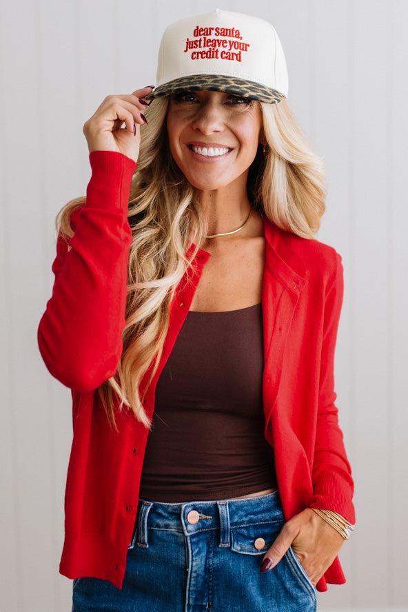 Blonde woman in dark jeans modeling in bright studio wearing a red cardigan with brown button front.