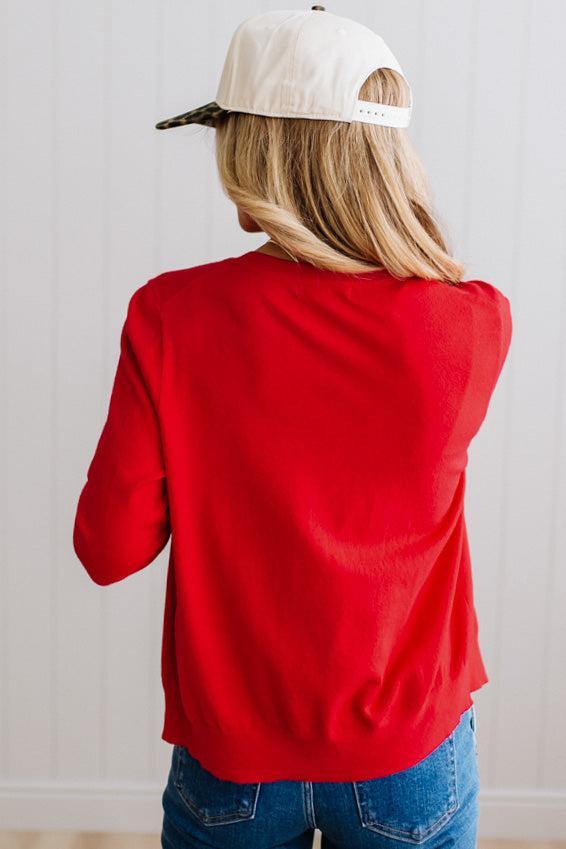 Blonde woman in dark jeans modeling in bright studio wearing a red cardigan with brown button front.