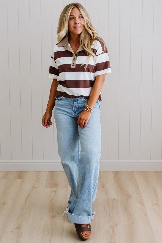 Woman wearing a striped shirt and jeans standing against a white paneled wall.