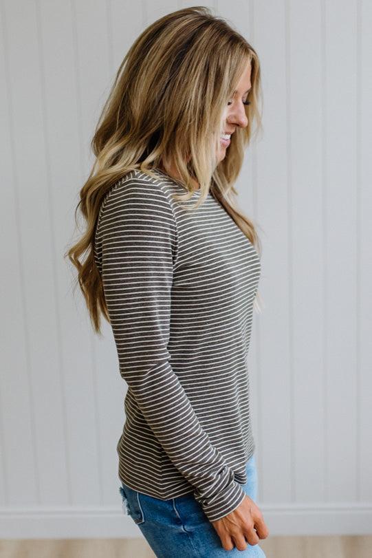 A woman modeling a long-sleeve striped knit top and blue jeans in a bright room with white paneled walls and light wood flooring.