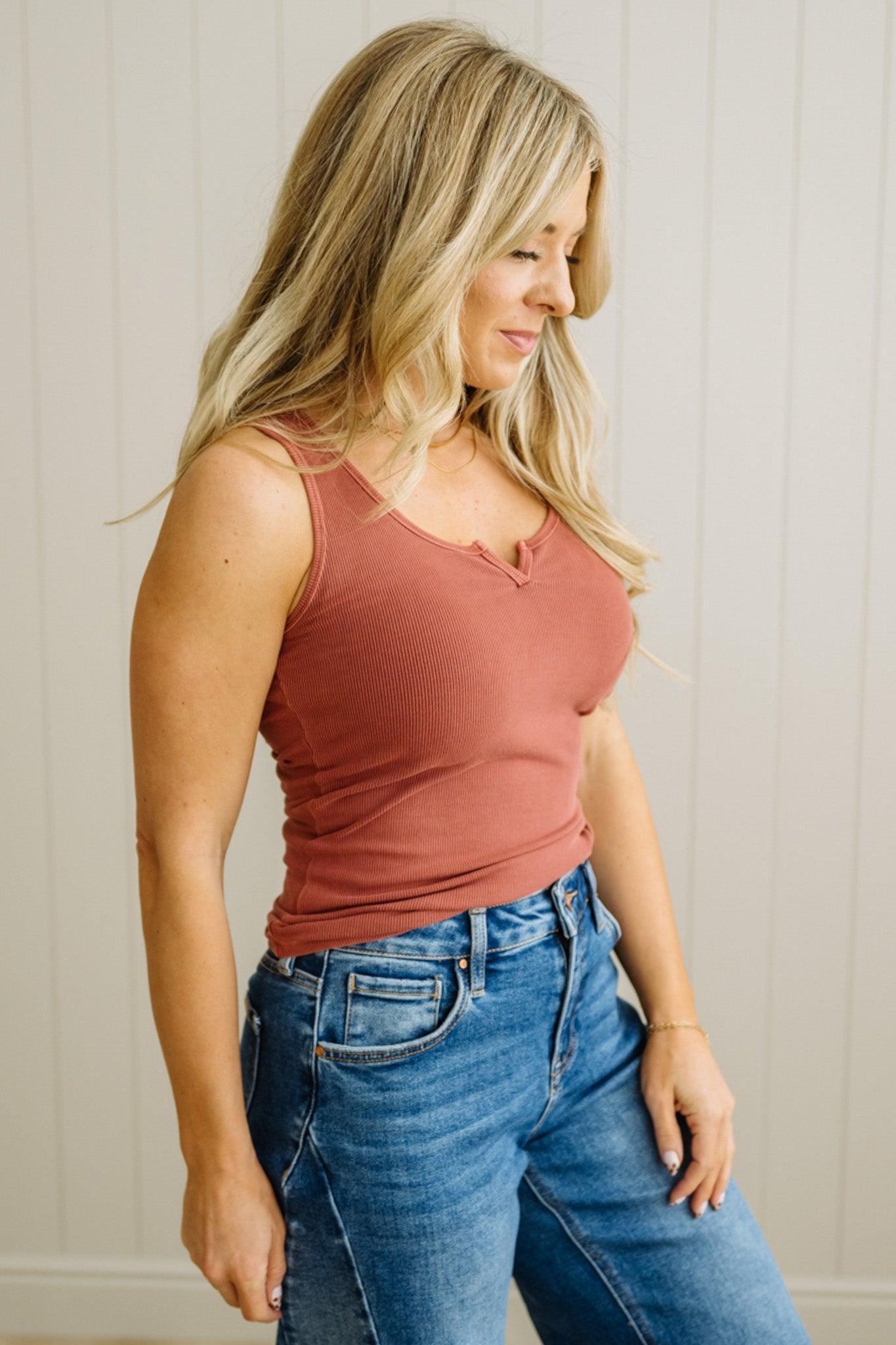 Woman wearing a rust-colored tank top and blue jeans against a neutral background