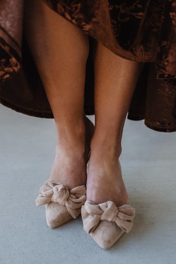 Beige shoes with bow details worn by a person in a brown dress.