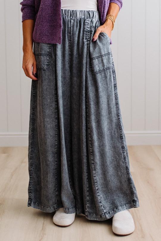 WOMAN IN A BRIGHTLY LIT STUDIO WEARING A TANK WITH CHAMBRAY ELASTIC WAIST POUCH POCKET WIDE LEG CULOTES PANTS IN GREY.