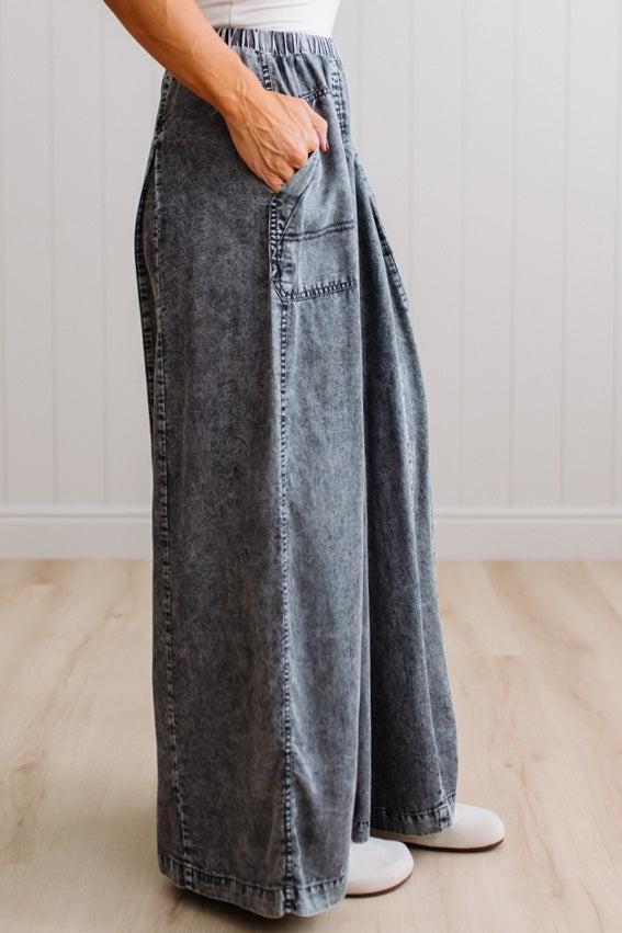 WOMAN IN A BRIGHTLY LIT STUDIO WEARING A TANK WITH CHAMBRAY ELASTIC WAIST POUCH POCKET WIDE LEG CULOTES PANTS IN GREY.