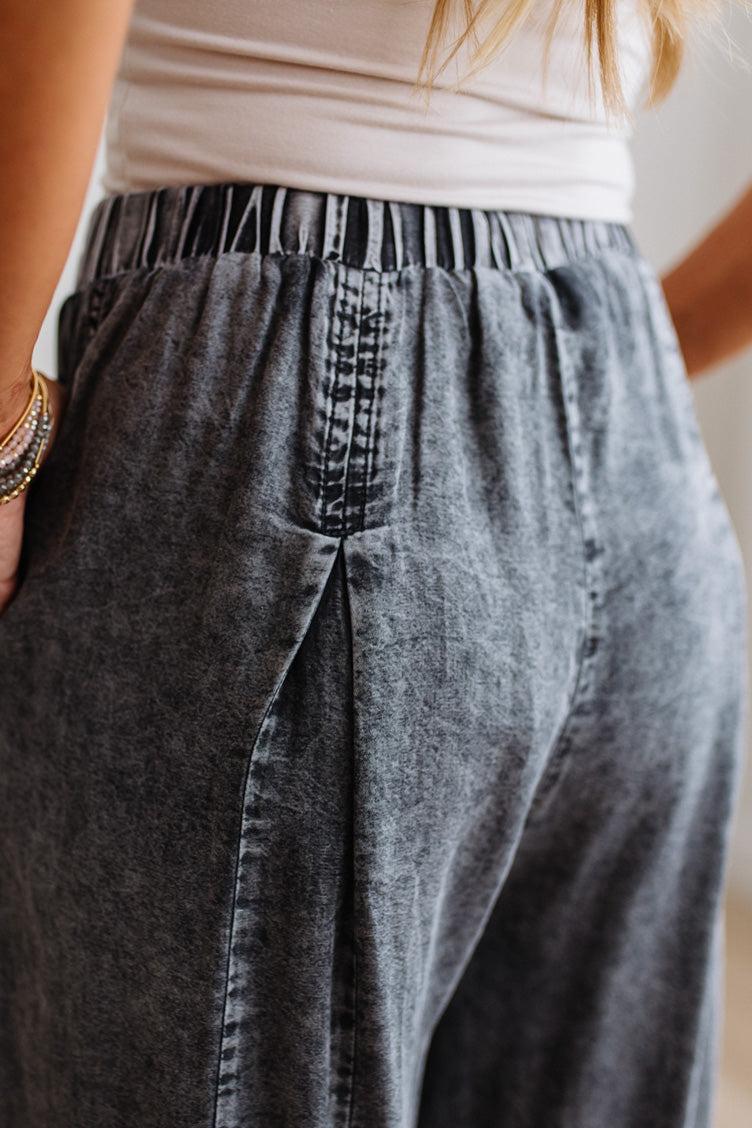 WOMAN IN A BRIGHTLY LIT STUDIO WEARING A TANK WITH CHAMBRAY ELASTIC WAIST POUCH POCKET WIDE LEG CULOTES PANTS IN GREY.