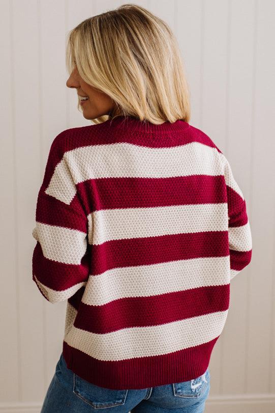 A woman wearing a knit sweater with horizontal burgundy and cream stripes, shown from the back against a light paneled wall.