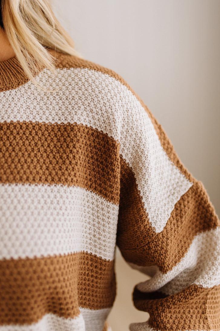 Close-up of a person wearing a chunky knit sweater with wide horizontal stripes in warm brown and off-white.