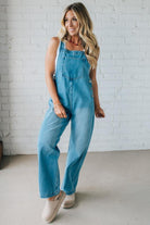 Woman wearing blue denim overalls against a white brick wall.