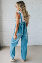 Woman wearing blue denim overalls against a white brick wall.