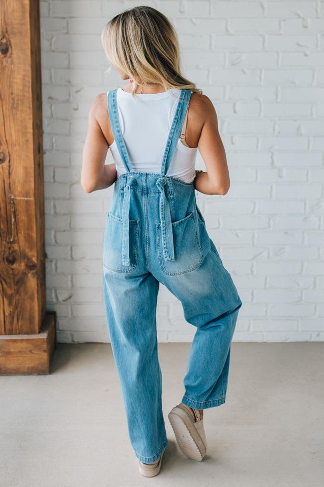 Person wearing blue denim overalls with a white brick wall background