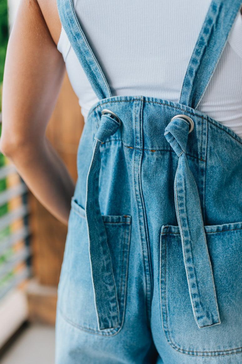 Close-up of a person wearing blue denim overalls with knot strap back detail on a blurred background