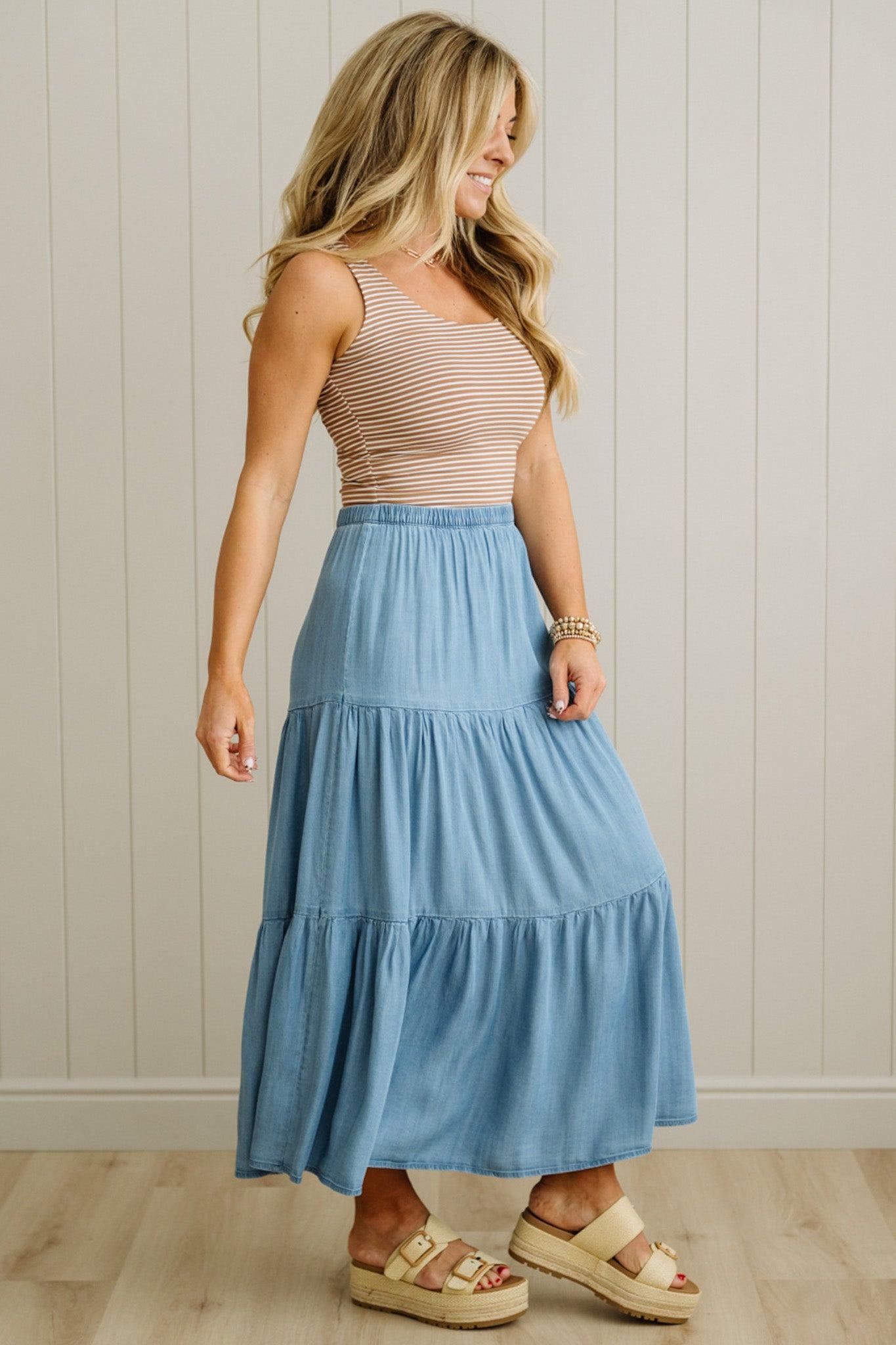 Woman wearing a striped tank top and blue tiered skirt against a neutral wall.