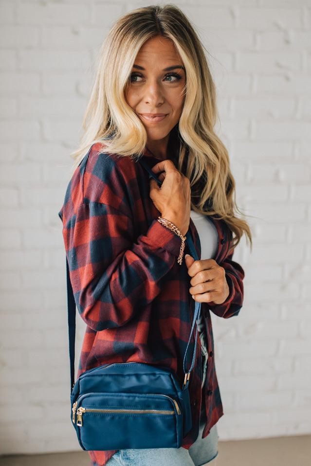 Woman wearing a red plaid shirt with a blue backpack against a white brick wall.