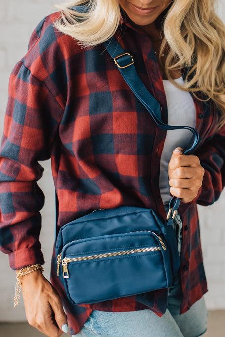 Person wearing a red and blue plaid shirt holding a blue crossbody bag.