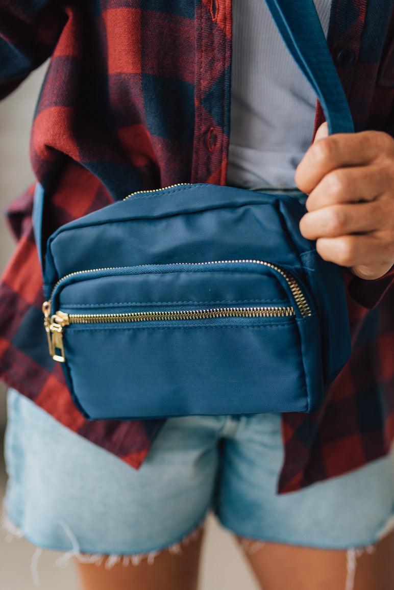 Person wearing a blue crossbody bag with a plaid shirt and denim shorts.