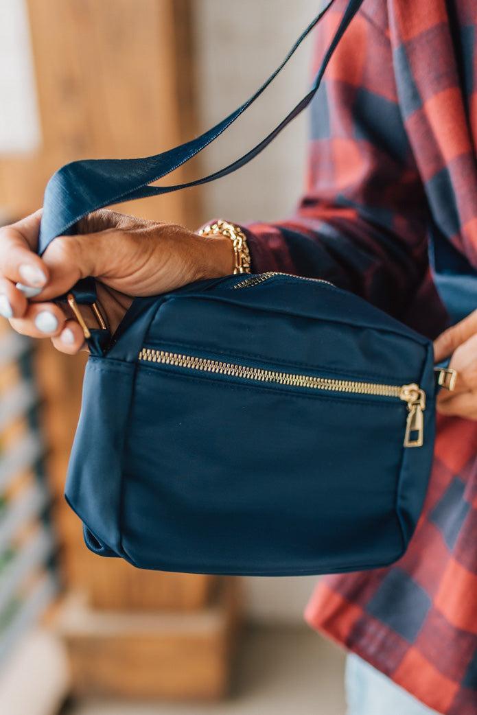 Person holding a navy blue handbag with gold zippers, wearing a plaid shirt.