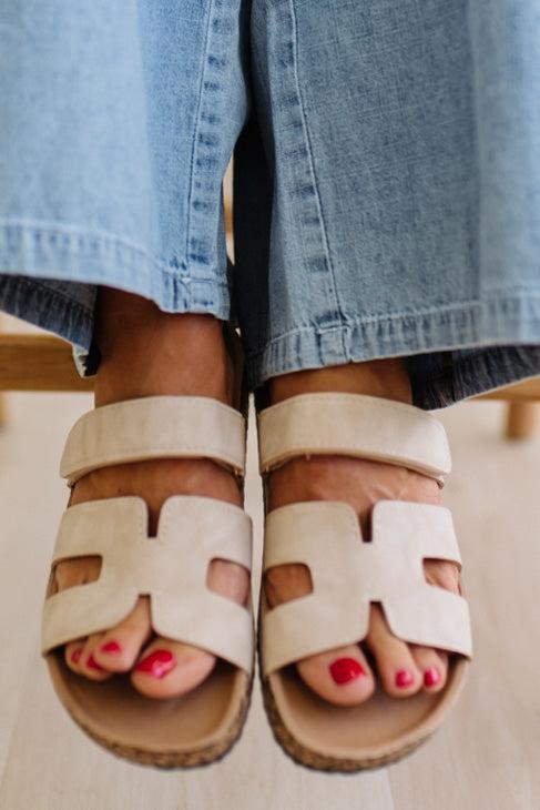 Beige sandals worn with blue jeans on a neutral background