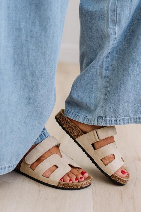 Close-up of feet wearing beige sandals with cork soles and blue jeans.