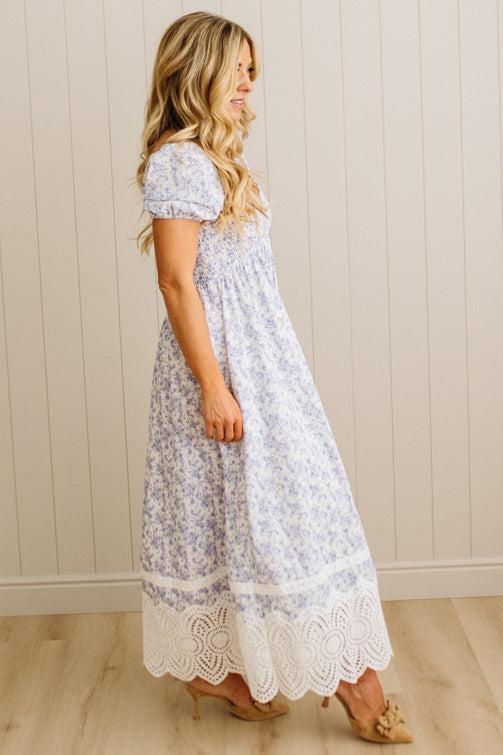 White dress with blue floral pattern and lace trim on a wooden floor.