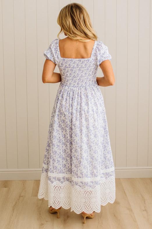 Woman wearing a floral dress with lace details, standing against a wooden paneled wall.