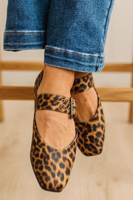 Leopard print flats with a gold buckle worn with rolled-up jeans on a neutral background