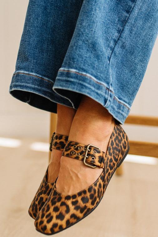 Leopard print flats with a gold buckle worn with rolled-up jeans on a neutral background