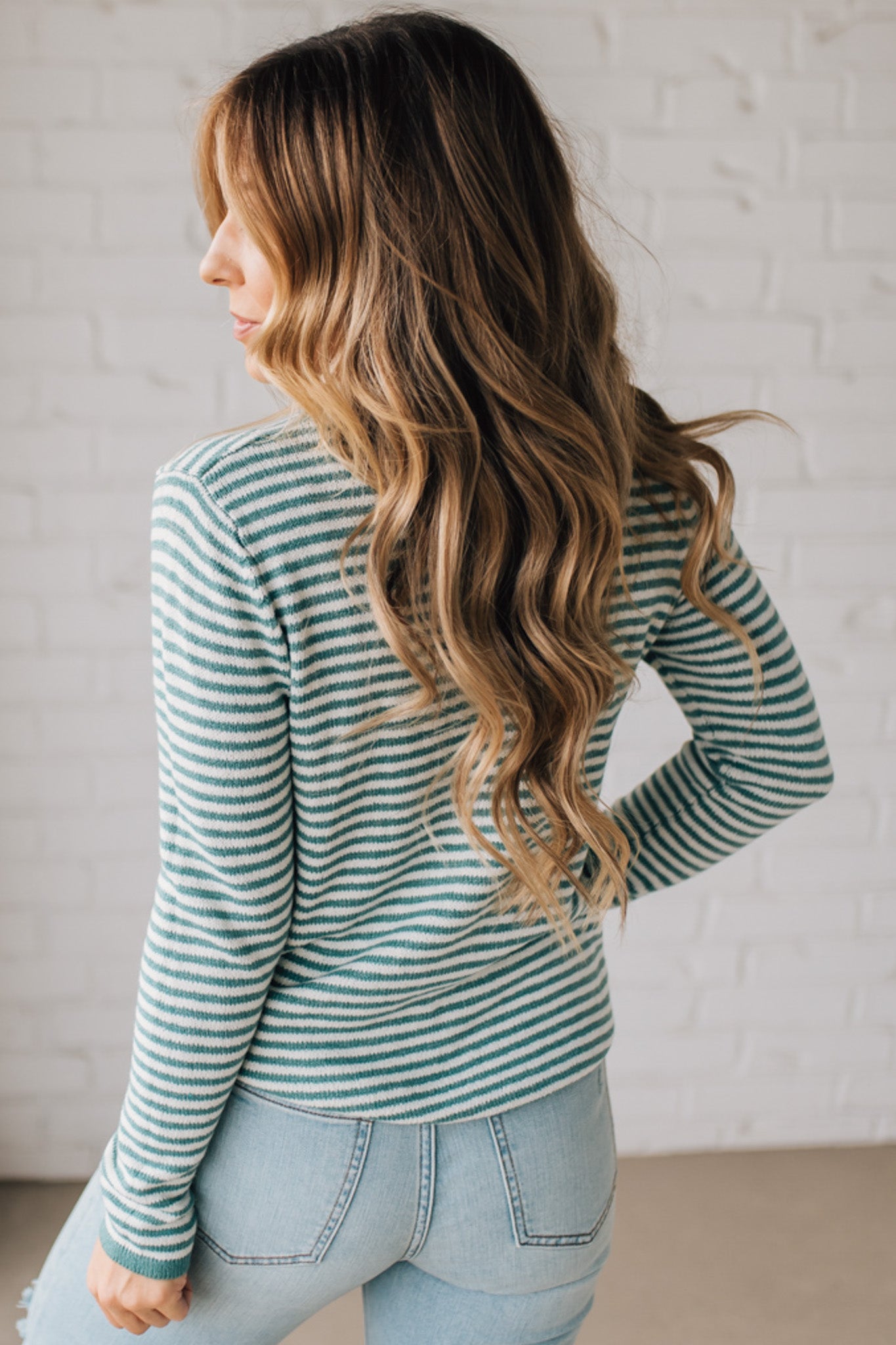 BLONDE WOMAN MODELING A LONG SLEEVE GREEN AND WHITE STRIPED SWEATER WITH SOLID GREEN ON THE NECKLINE AND SLEEVE CUFFS
