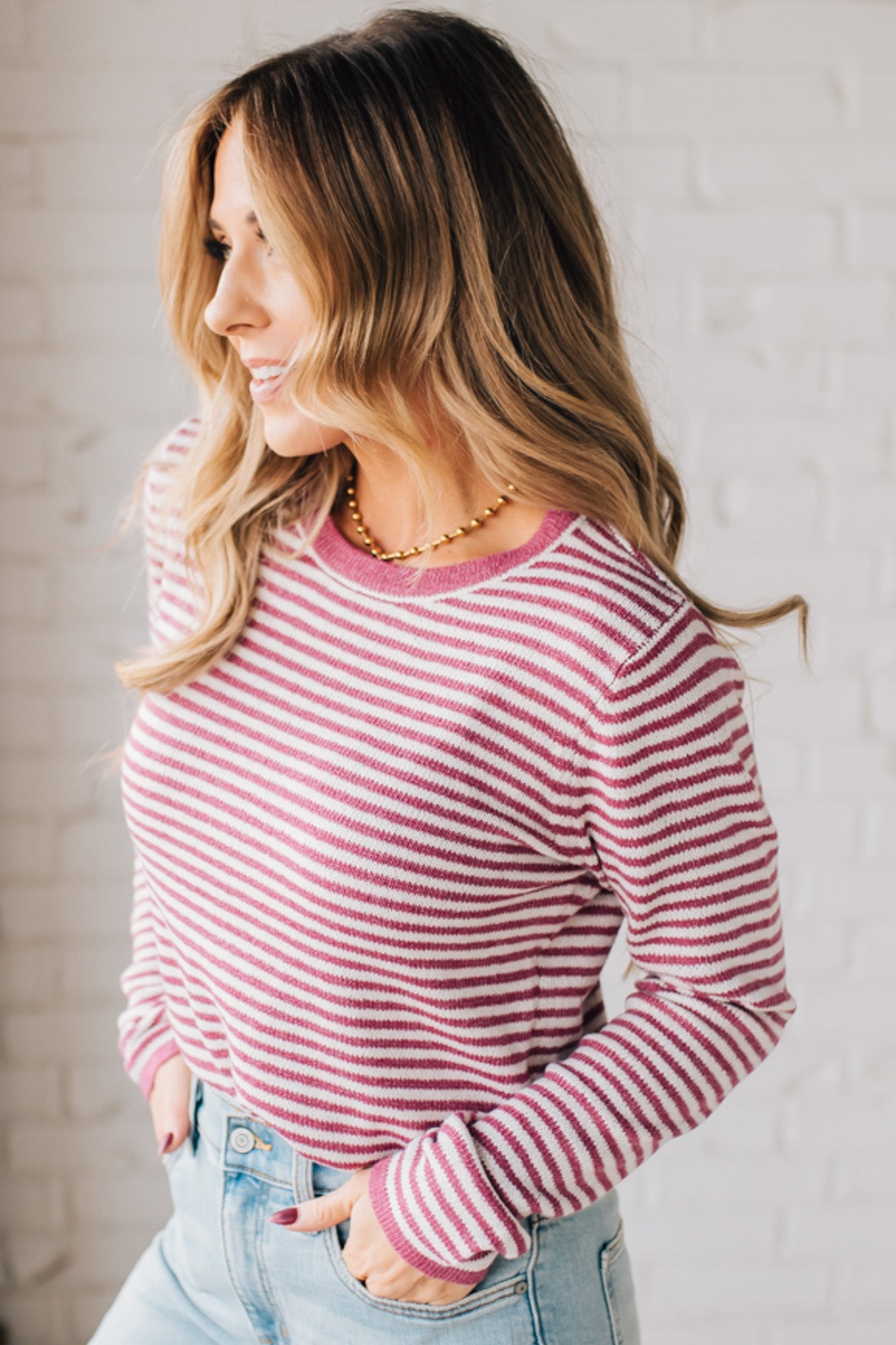 BLONDE WOMAN MODELING A LONG SLEEVE MAGENTA AND WHITE STRIPED SWEATER WITH SOLID MAGENTA ON THE NECKLINE AND SLEEVE CUFFS