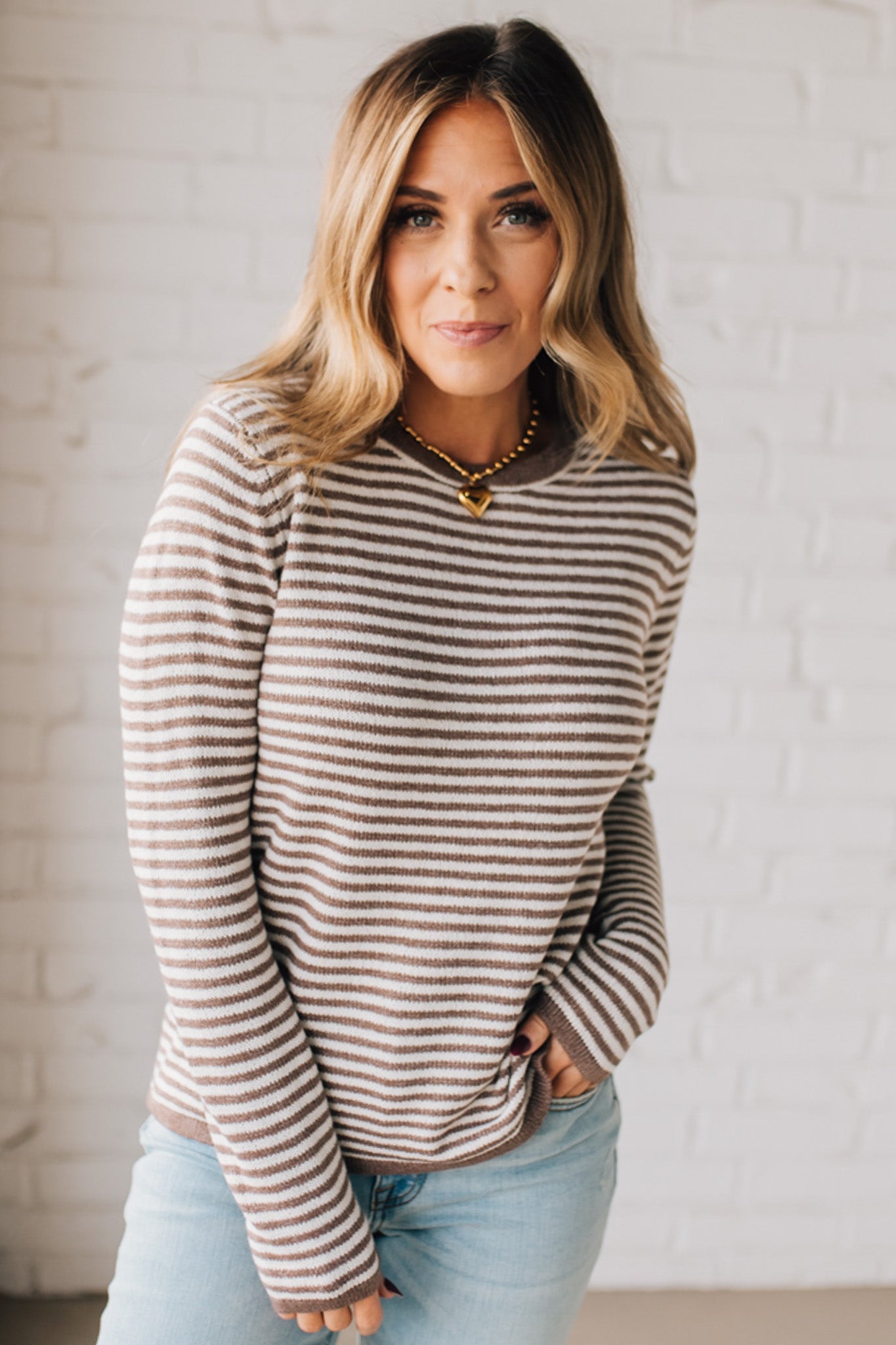 BLONDE WOMAN MODELING A LONG SLEEVE MOCHA AND WHITE STRIPED SWEATER WITH SOLID MOCHA ON THE NECKLINE AND SLEEVE CUFFS