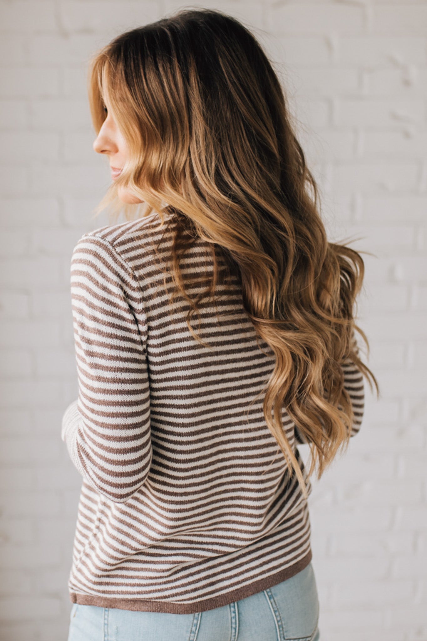 BLONDE WOMAN MODELING A LONG SLEEVE MOCHA AND WHITE STRIPED SWEATER WITH SOLID MOCHA ON THE NECKLINE AND SLEEVE CUFFS