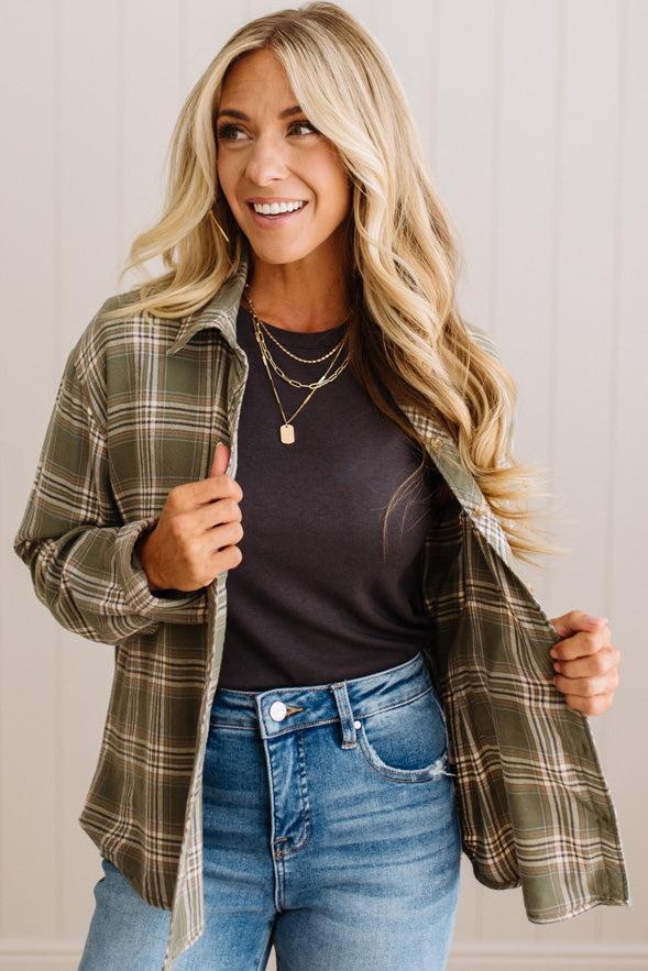 Blonde woman wearing a grey shirt with an opened olive green plaid flannel button up top over.
