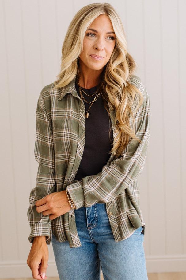 Blonde woman wearing a grey shirt with an opened olive green plaid flannel button up top over.