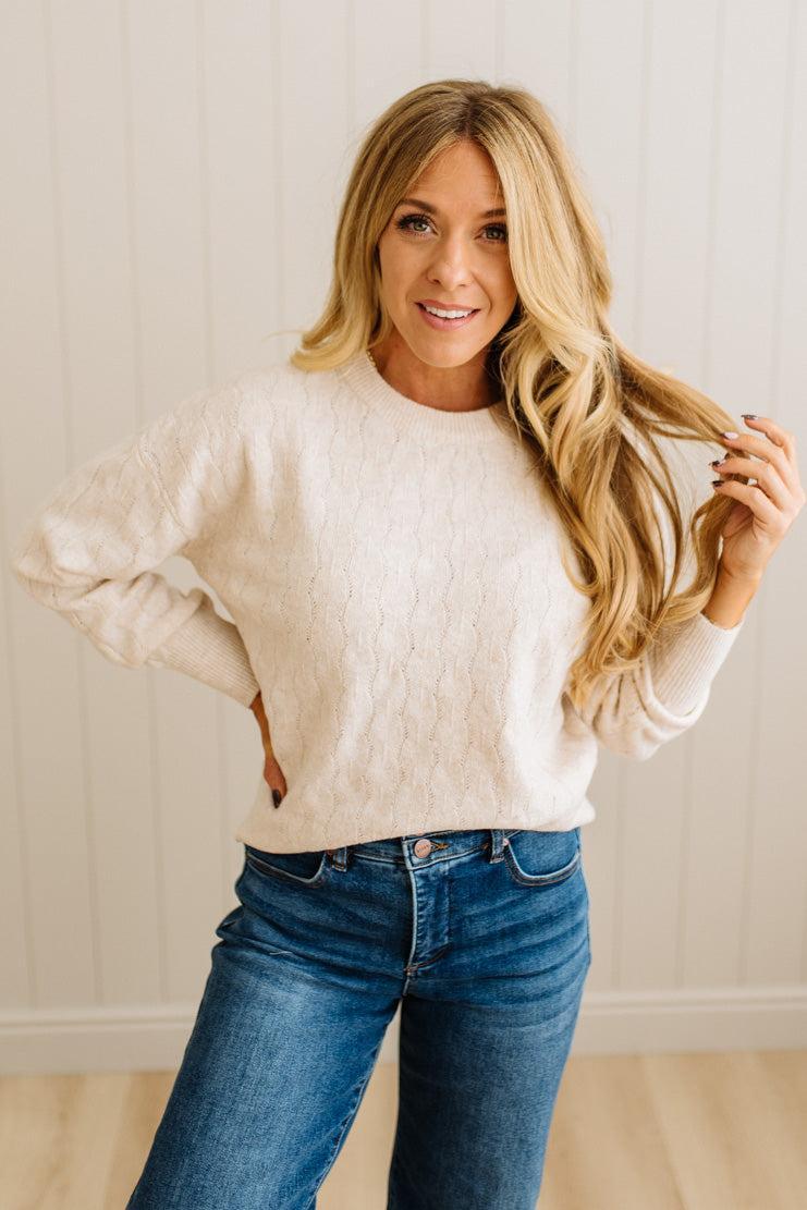 Woman wearing a white sweater and blue jeans against a light background