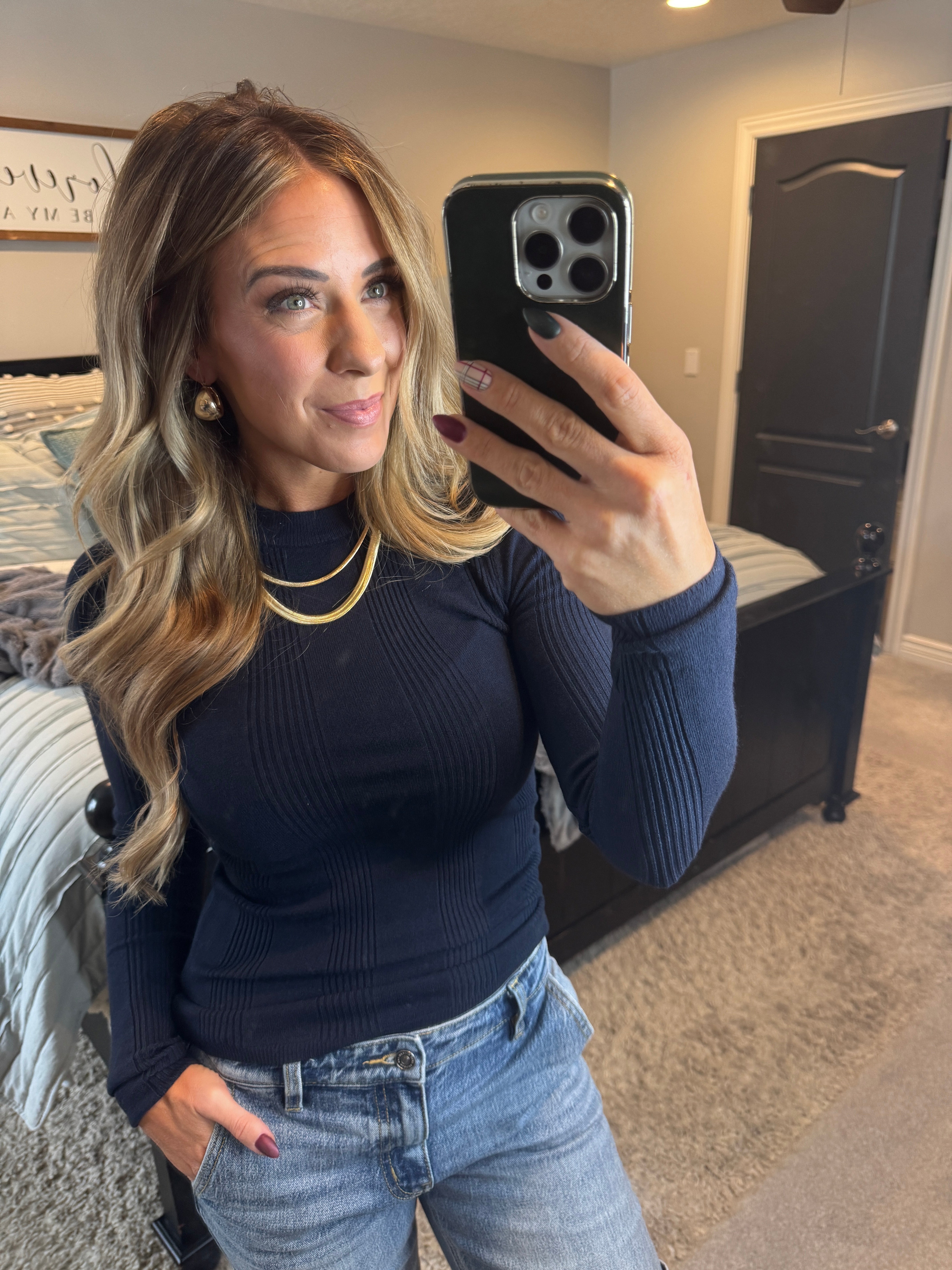 A woman wearing a solid, ribbed, slim fit sweater with a round neck, long sleeves, and tucking it into high-waisted jeans.