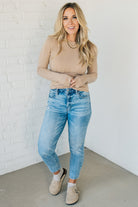 A woman wearing a solid, ribbed, slim fit sweater with a round neck, long sleeves, and tucking it into high-waisted jeans.