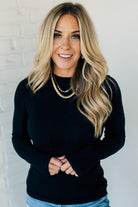 A woman wearing a navy, ribbed, slim fit sweater with a round neck, long sleeves, and tucking it into high-waisted jeans.