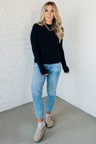 A woman wearing a solid, ribbed, slim fit sweater with a round neck, long sleeves, and tucking it into high-waisted jeans.