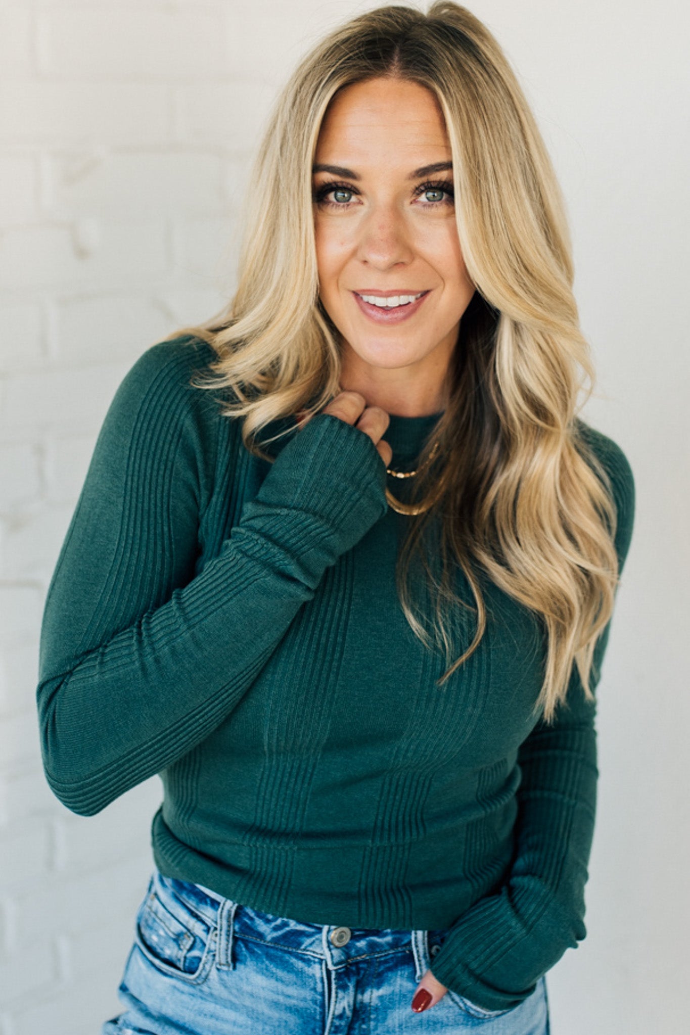 A woman wearing a solid, ribbed, slim fit sweater with a round neck, long sleeves, and tucking it into high-waisted jeans.