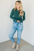 A woman wearing a solid, ribbed, slim fit sweater with a round neck, long sleeves, and tucking it into high-waisted jeans.