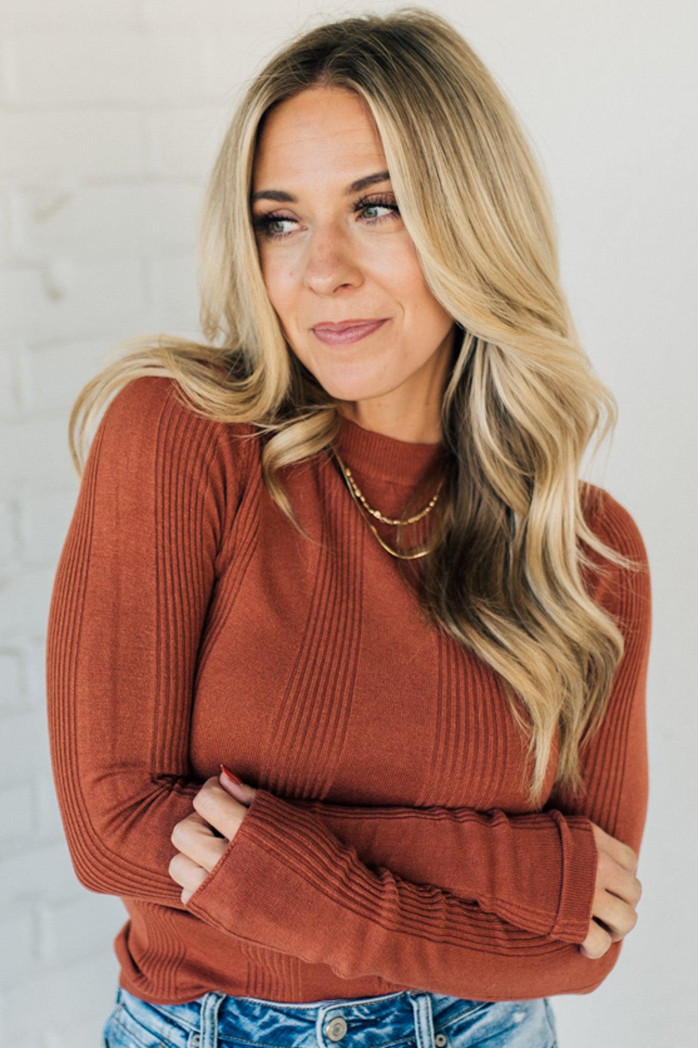 A woman wearing a solid, ribbed, slim fit sweater with a round neck, long sleeves, and tucking it into high-waisted jeans.