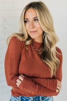 A woman wearing a solid, ribbed, slim fit sweater with a round neck, long sleeves, and tucking it into high-waisted jeans.