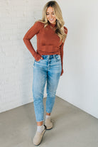 A woman wearing a solid, ribbed, slim fit sweater with a round neck, long sleeves, and tucking it into high-waisted jeans.