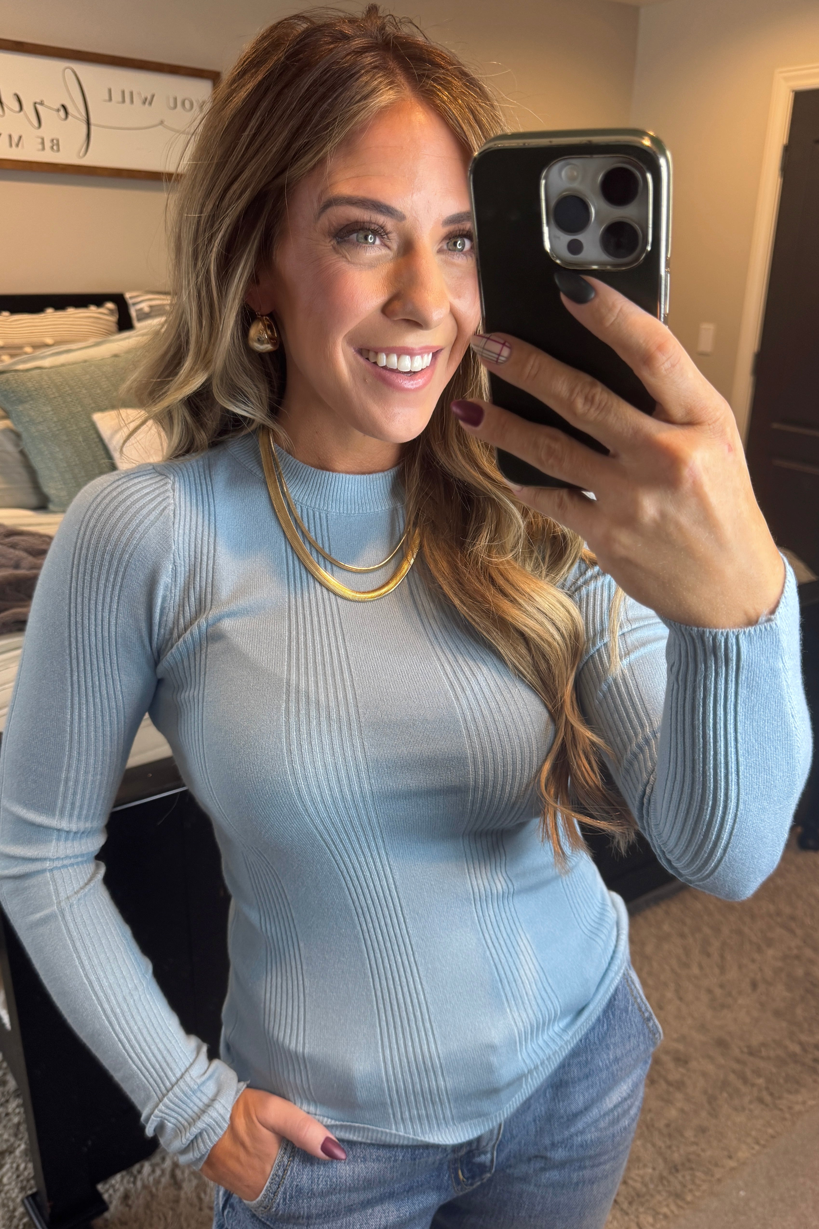 A woman wearing a solid, ribbed, slim fit sweater with a round neck, long sleeves, and tucking it into high-waisted jeans.