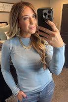 A woman wearing a navy, ribbed, slim fit sweater with a round neck, long sleeves, and tucking it into high-waisted jeans.