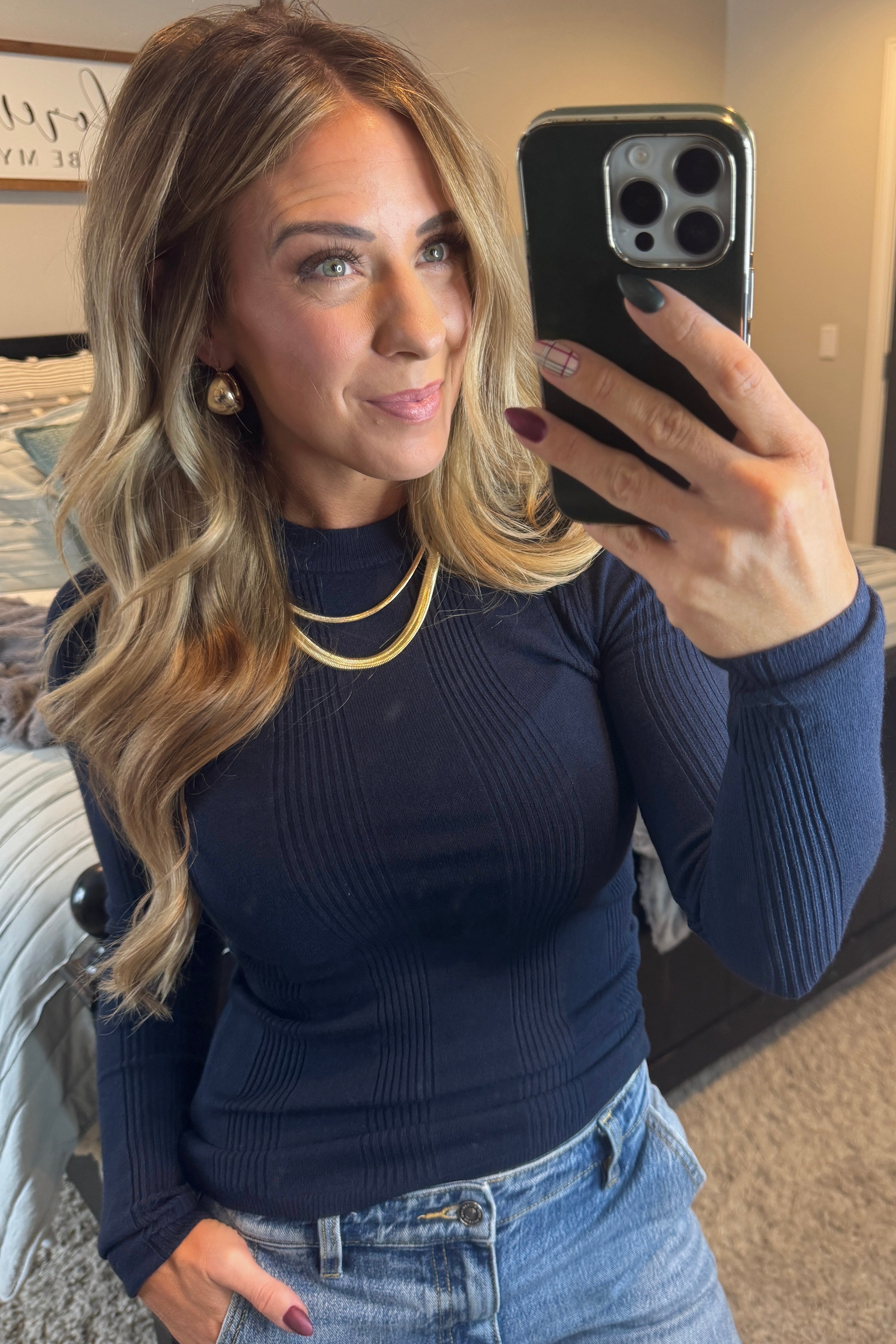 A woman wearing a solid, ribbed, slim fit sweater with a round neck, long sleeves, and tucking it into high-waisted jeans.