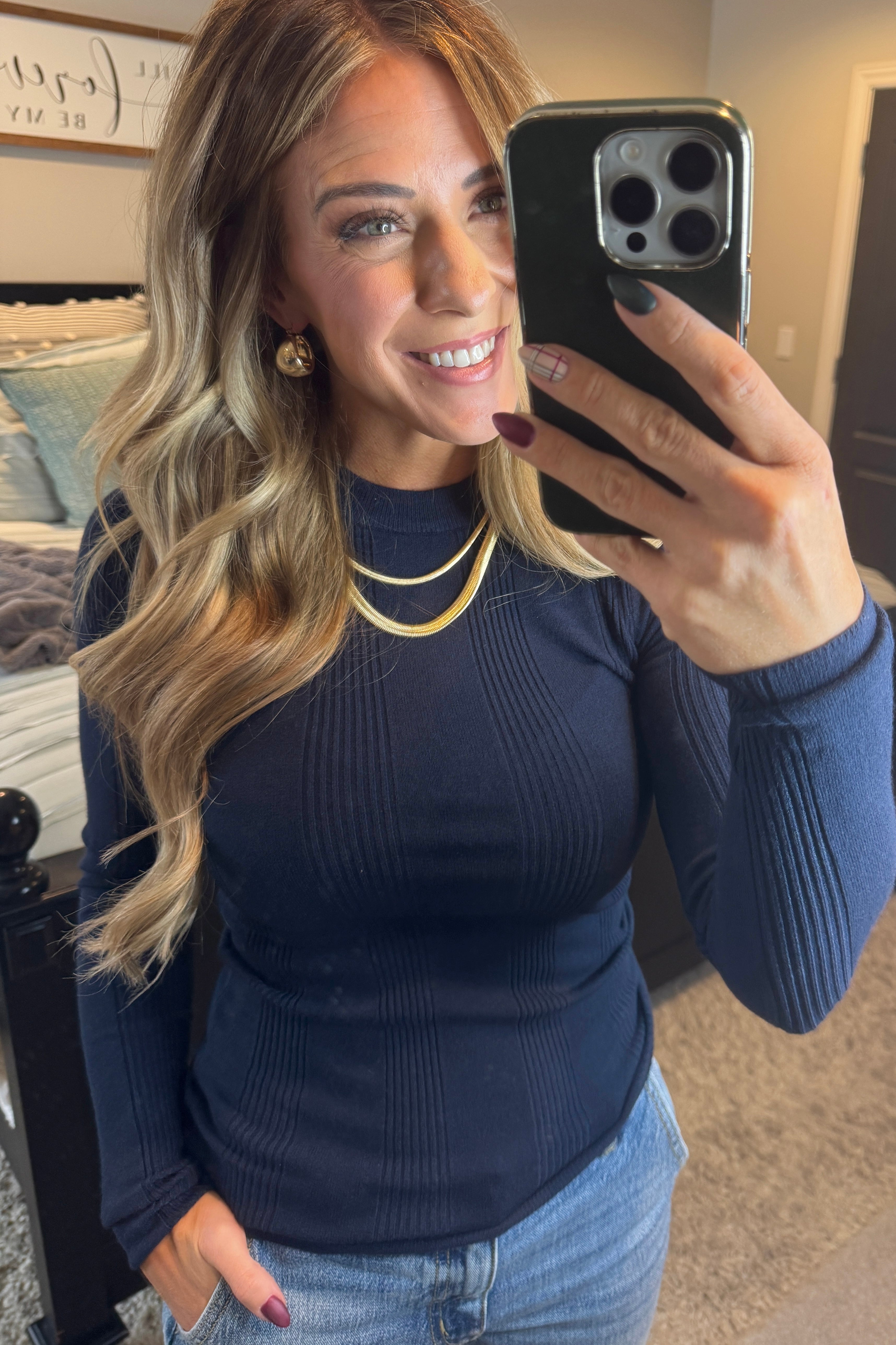 A woman wearing a navy, ribbed, slim fit sweater with a round neck, long sleeves, and tucking it into high-waisted jeans.