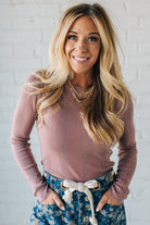 Woman wearing a ribbed long-sleeve top and floral pants against a white brick wall.