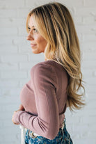 Woman wearing a pink ribbed sweater against a white brick wall