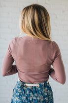 Person wearing a pink ribbed sweater and floral skirt against a white wall