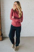Woman wearing a red sweater and dark jeans standing against a white brick wall.